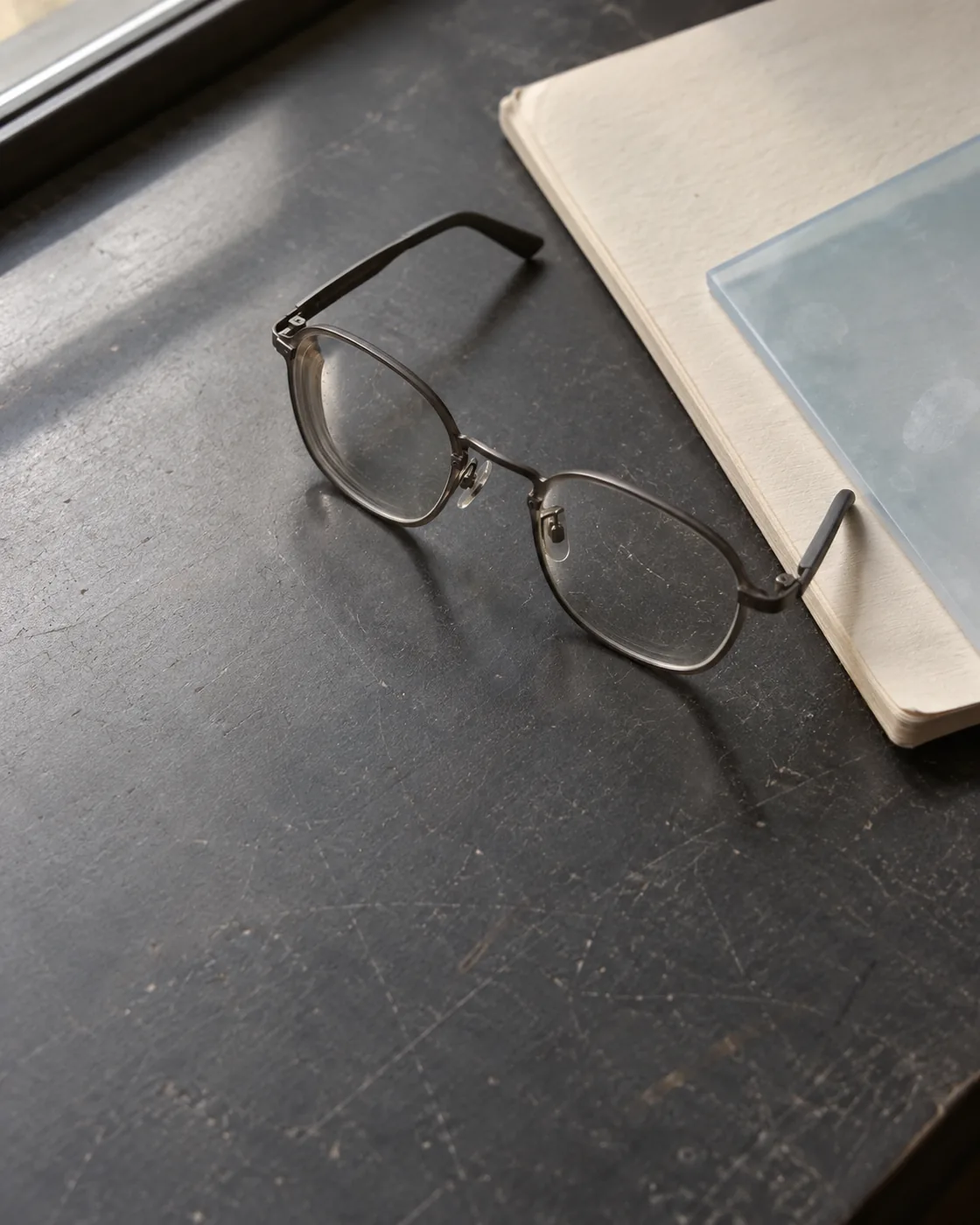 Reading glasses beside notebooks and pale-blue acetate on a worn work desk